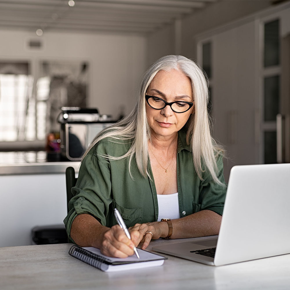 woman writing notes while using laptop