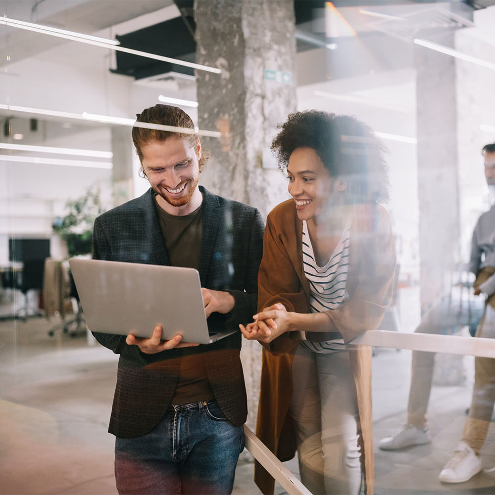 two coworkers smiling while looking at laptop