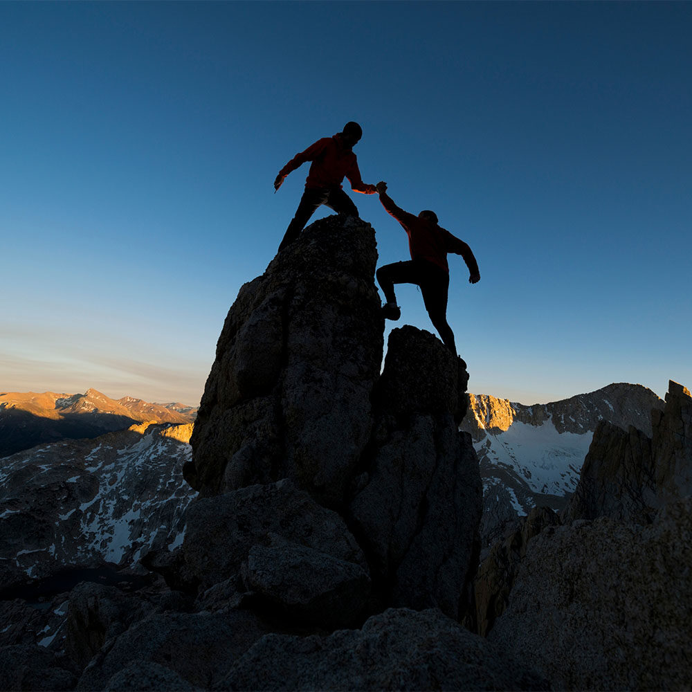 climber helping another to the top of a peak